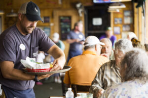 Male Server with cap delivering appetizers to a table to their delight.