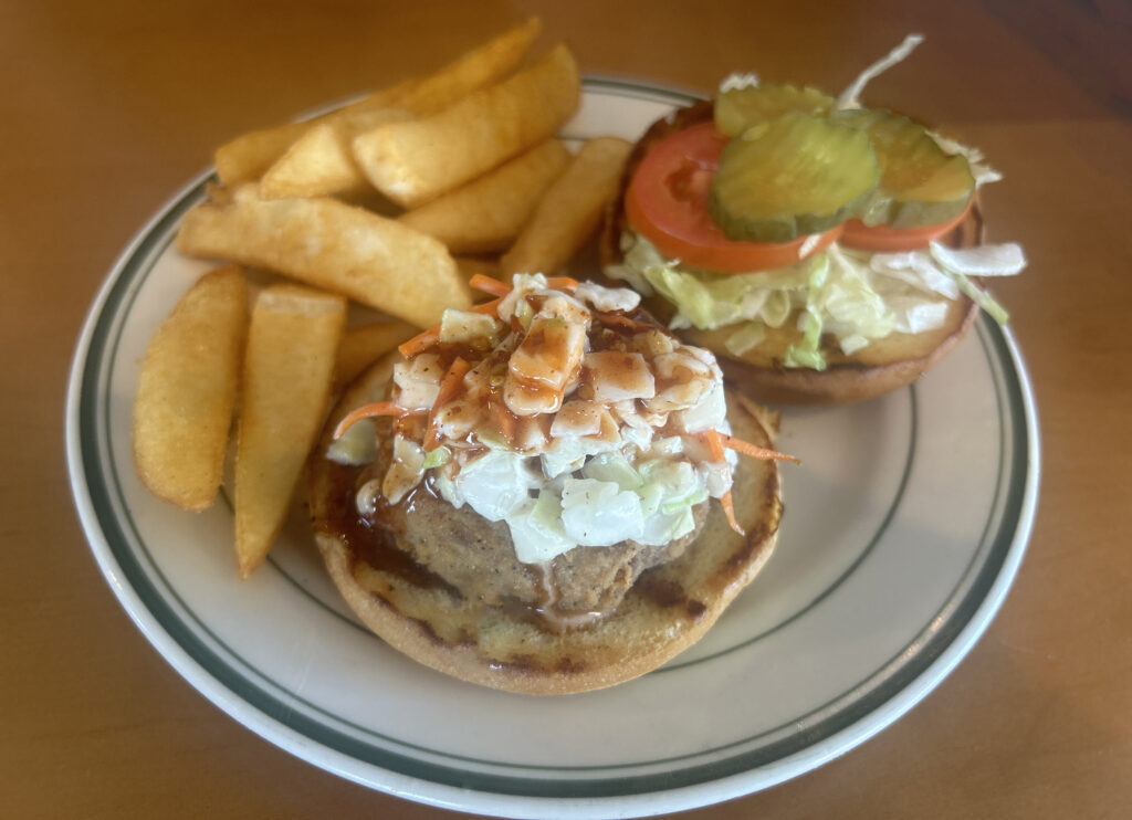 Billie Gs Crabby Patty open-faced sandwich on brioche bun, topped with sweet slaw and spicy sauce. Served with choice of 1 side.